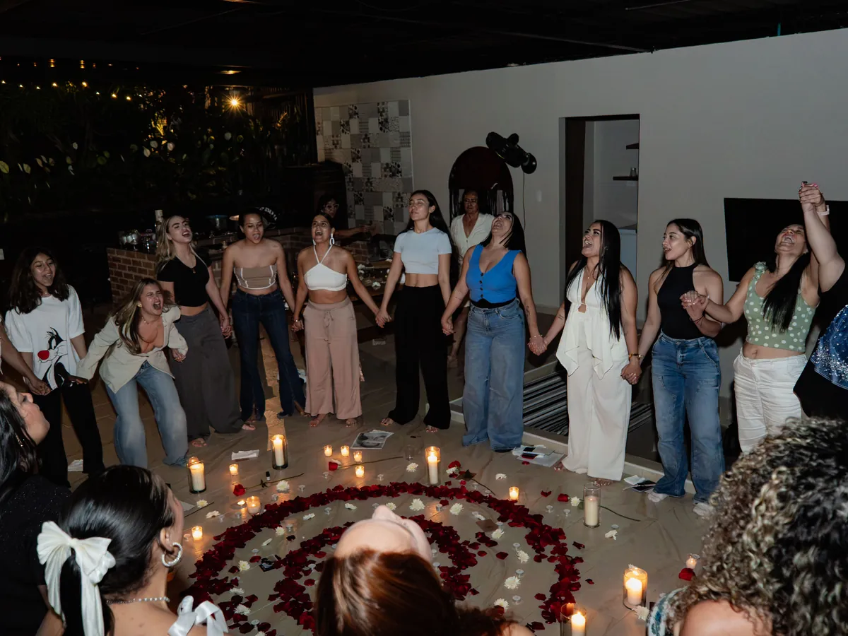 Un círculo de mujeres tomadas de la mano alrededor de velas y pétalos de rosa